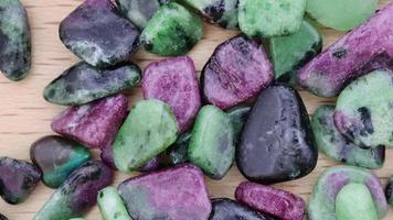 Ruby zoisite jewel stones heap up texture on light varnished wood background. Moving right seamless loop backdrop. video