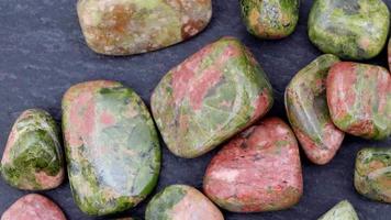 Unakite heap up jewel stones texture on black stone background. Moving right seamless loop backdrop. video