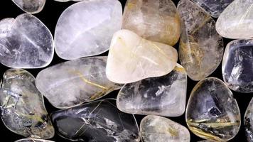 Rutilated quartz heap jewel stones texture on black background. Moving right seamless loop backdrop. video