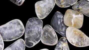 Rutilated quartz heap up jewel stones texture on black background. Moving right seamless loop backdrop. video