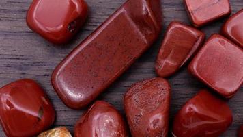 Red jasper heap up jewel stones texture on brown varnished wood background. Moving right seamless loop backdrop. video