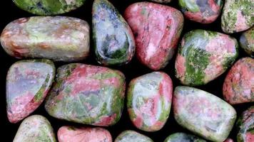 Unakite heap jewel stones texture on black background. Moving right seamless loop backdrop. video