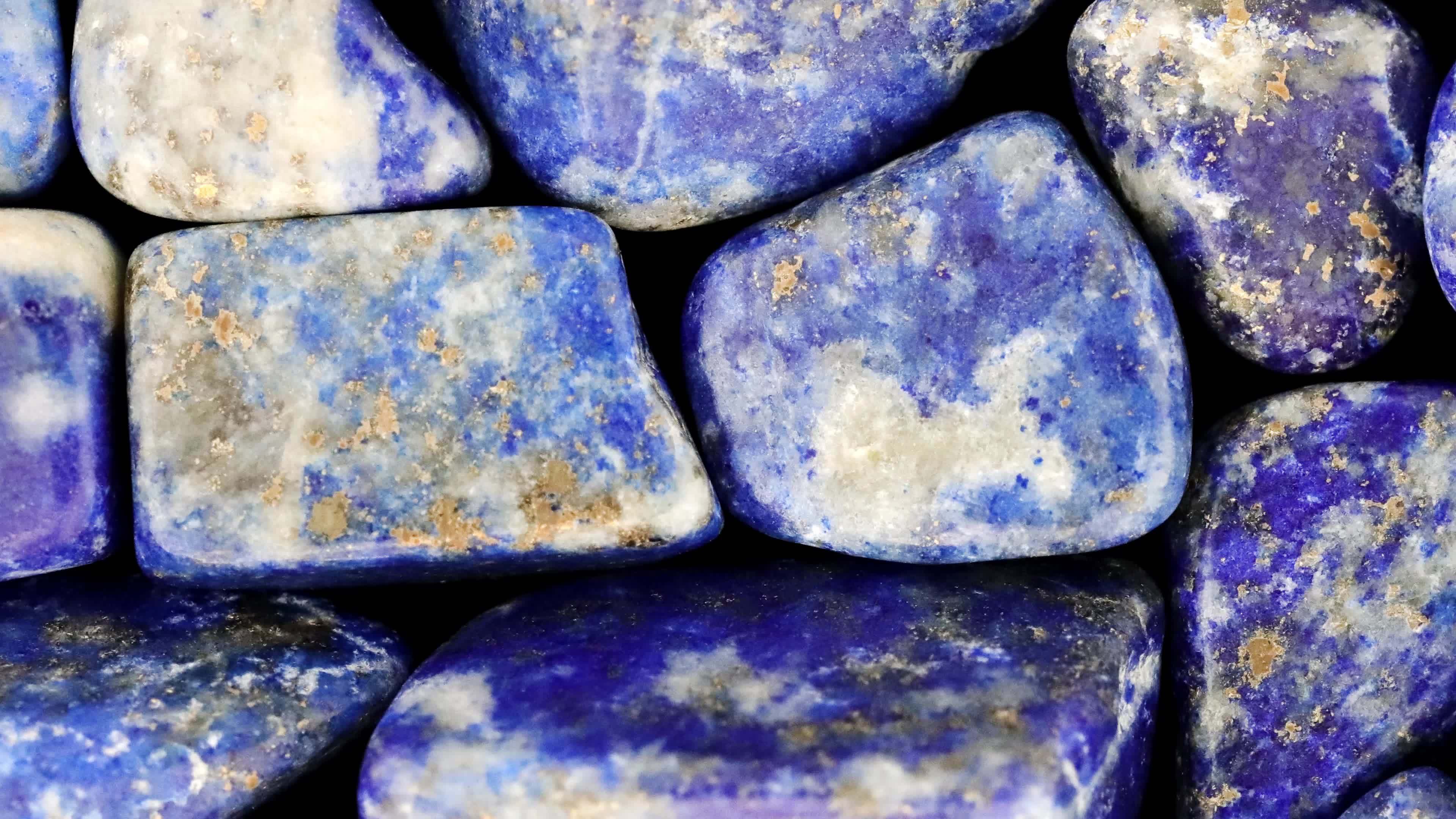Lapis lazuli heap jewel stones texture on black background. Moving