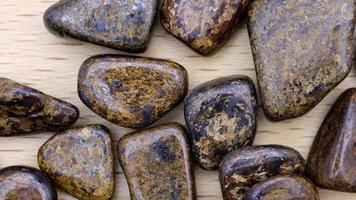 Bronzite heap up jewel stones texture on light varnished wood background. Moving right seamless loop backdrop. video