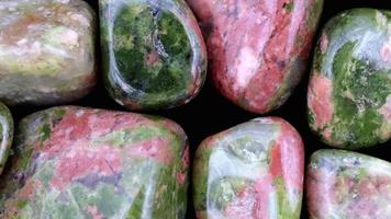 Unakite heap jewel stones texture on black background. Moving right seamless loop backdrop. video