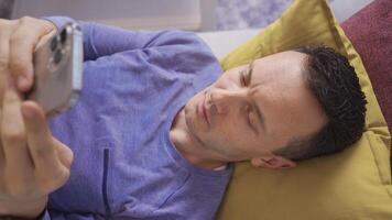 Sleepy man drops phone from his hand. The man looking at the phone while lying down drops the phone on his face. video