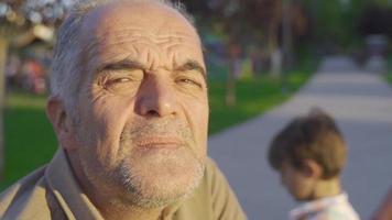 vecchio pensionato uomo prendere il sole. uomo seduta all'aperto nel il parco è seduta contro il sole. video