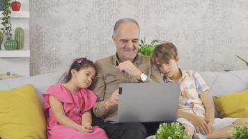 farfar och barnbarn ser på bärbar dator skärm. morfar ser på bärbar dator skärm med hans barnbarn. video