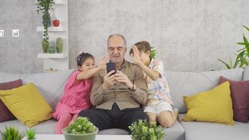 de opa met zijn kleinkinderen is videogesprekken Aan zijn telefoon. video