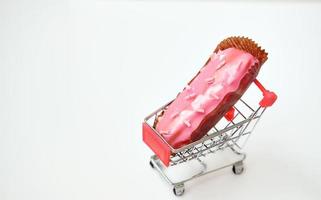 carrito de compras lleno de regalos. comprando postre. eclair rosa en una cesta foto