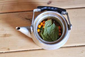 Tea with sea buckthorn berries in an iron teapot on a wooden background, top view, copy space. Seasonal autumn spicy sea buckthorn tea. photo