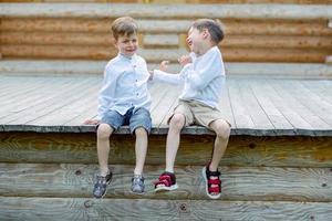 children are sitting on the bench. 2 brothers are fooling around. friends are playing. children laugh photo