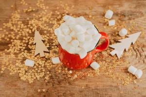 Gold sparkles and a cup of coffee with marshmallows on a wooden background. Christmas background made of sparkles and red cups with cocoa photo