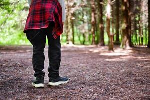 young man walking in the park. Close up view on man's legs in jeans and black leather boots with sunlight against nature blur background. photo