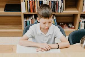 Schoolboy sitting on table and reading book in library at school. Preparing for homework. a good student. The boy loves to read. Free space at the school photo