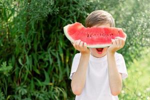 Portrait of teen boy eating ripe juicy watermelon and smiling. Cute caucasian young teenager. Funny happy child covered his face with slice red watermelon. photo