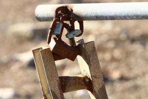 A rusty padlock hangs on a closed gate. photo