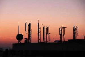 silueta de transmisores gsm en el edificio de oficinas del techo al atardecer foto