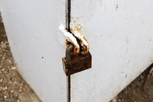 A rusty padlock hangs on a closed gate. photo