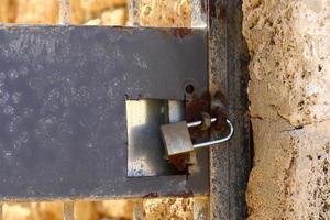 A rusty padlock hangs on a closed gate. photo