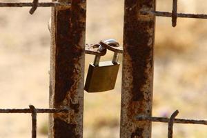 A rusty padlock hangs on a closed gate. photo