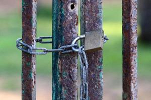 A rusty padlock hangs on a closed gate. photo