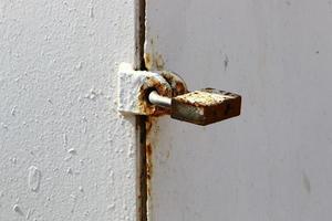 A rusty padlock hangs on a closed gate. photo
