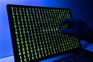Hacked or hacking computer concept. Gloved Hand, Binary code and hacked word on laptop computer screen photo