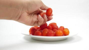 A hand picks a small tomato from plate, cherry tomatoes video