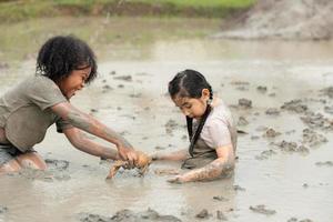 los niños se divierten jugando en el lodo en los campos comunitarios y atrapando una rana en un lodo. foto