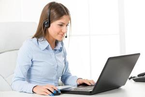 mujer de negocios con auriculares, escribiendo en la computadora portátil foto