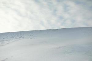 Snowy slope against sky. Avalanche of snow on mountain ridge. Winter weather. photo
