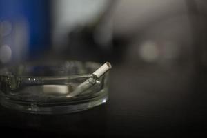 Cigarette in ashtray. Smoking is harmful to health. Glass ashtray on table.