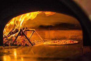 Pizza near the stone stove with fire. Background of a traditional pizzeria restaurant with a fire place. photo