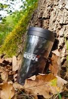 KRAKOW, POLAND, 2020 - Black thermos mug with Nescafe logo lies on fallen foliage at the foot of the oak tree. A hot drink at a picnic in the autumn forest. photo