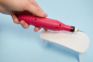 The process of making a beautiful manicure on the hands on the fingers with the help of a special machine and a lamp for drying the varnish in the nail beauty salon on a blue background photo