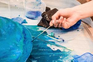 The process of creating a home-made trendy abstract modern pattern painted with a brush of acrylic blue multi-colored resin on a round wooden board photo