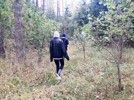 gente, recolectores de hongos con ropa abrigada caminan en una caminata por el bosque de otoño con árboles en la naturaleza a lo largo de la hierba y las hojas foto