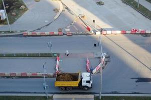 A large dump truck rides to a construction site and carries sand along an asphalt road. View from above photo