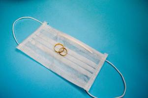 Gold wedding wedding rings lie on a disposable protective medical mask for protection against dangerous deadly diseases of microbes and viruses by the coronavirus covid-19 on a blue background photo