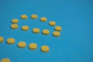 yellow pills are laid out on a colored blue background in the form of round letters. volumetric inscriptions on the background are photographed from the side. unusual perspective photo