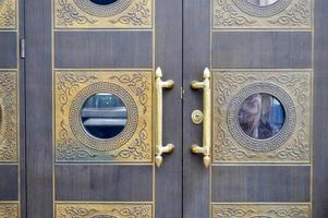 Texture of old decorative beautiful wooden door gates with patterned ornaments and gold ornaments, elements and gold door handles. The background photo