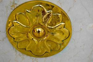 textura de una decoración redonda de metal dorado de un elemento de diseño de lujo con un patrón de flores contra una pared de piedra de mármol blanco. el fondo foto