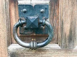 martinete de puerta de metal negro, pomo de puerta con un anillo para llamar al fondo de una antigua puerta marrón de madera foto