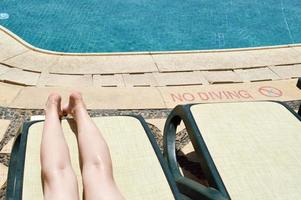 hermosas piernas, pies de chicas, mujeres en el fondo de una tumbona y piscina en un balneario tropical cálido y exótico, vacaciones de verano foto
