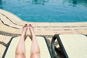 Beautiful legs, girls feet, women with red manicure on the backdrop of a deckchair and pool on a tropical warm exotic seaside resort, summer vacation photo