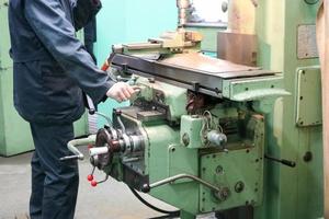 A male worker works on a larger metal iron locksmith lathe, equipment for repairs, metal work in a workshop at a metallurgical plant in a repair production photo