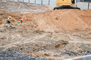 los trabajadores de la construcción, hombres con cascos y túnicas, cavan un agujero en la zanja manualmente con palas en un sitio de construcción foto