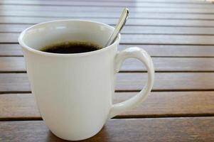 A white ceramic cup with a morning refreshing hot coffee with tea drink and tea shiny teaspoon is on a wooden table in a cafe photo