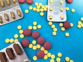 bright yellow, brown, red and pink tablets of a round and oval shape lie apart on a pink paper background. medical background from various drugs poured from a bottle photo